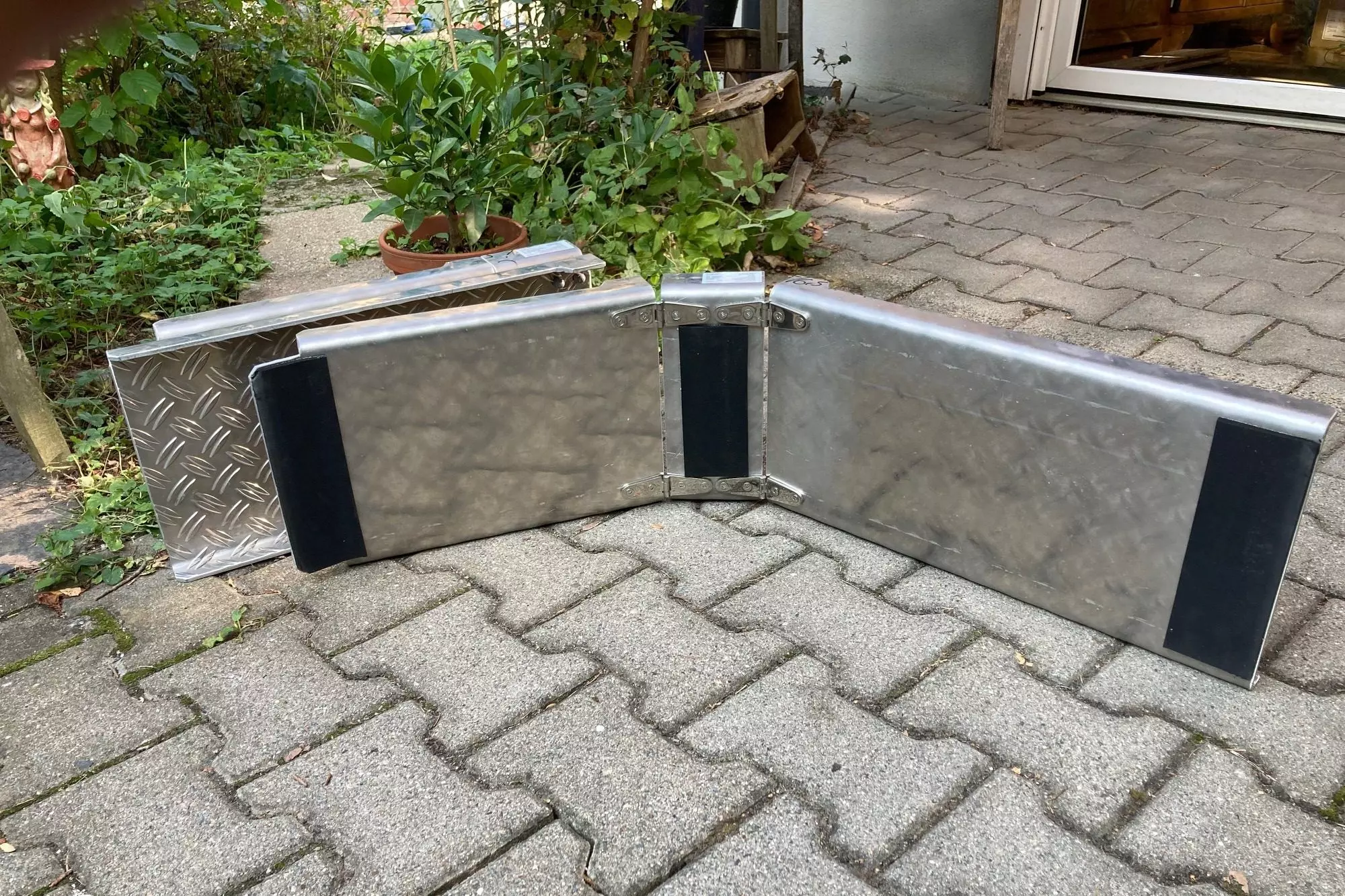Faltbare Alurampen für Rollstuhl oder Lasten mit verklebten Antirutschmatten an beiden Enden und in der Mitte der Unterseite. Fest verklebte Antirutschmatten an beiden Enden und in der Mitte der Unterseite an der Rollstuhlrampe.
